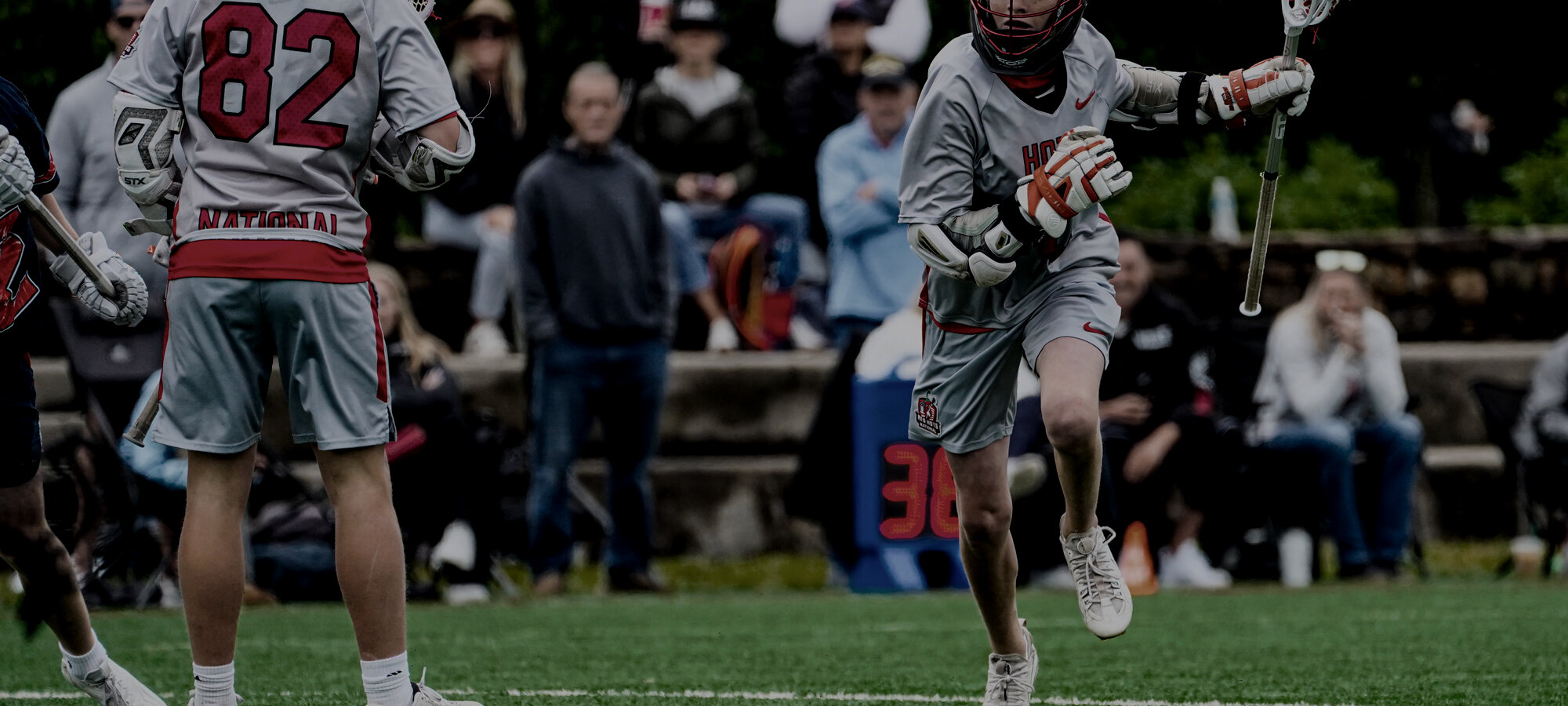 Club lacrosse players competing in front of a crowd.